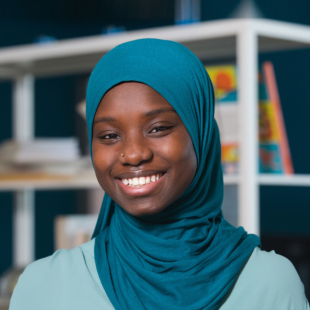 Headshot of Cesay Camara smiling in front of a bookshelf.