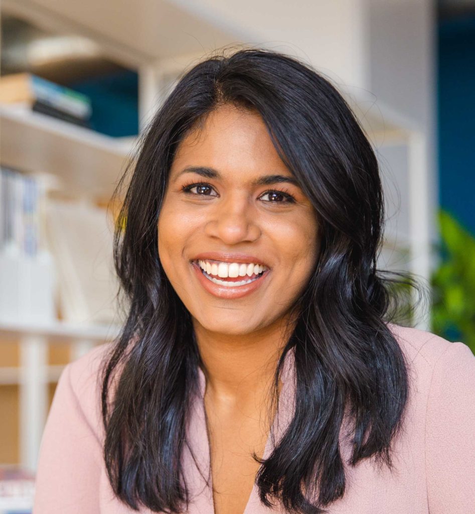 Headshot of Shanti Mathew smiling in front of a bookshelf.