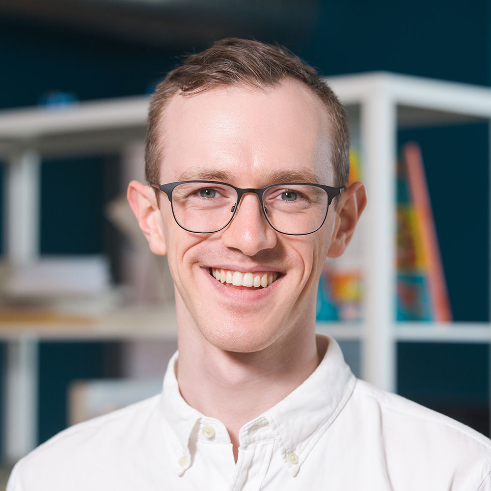 Headshot of Tim Duschenes smiling in front of a bookshelf.