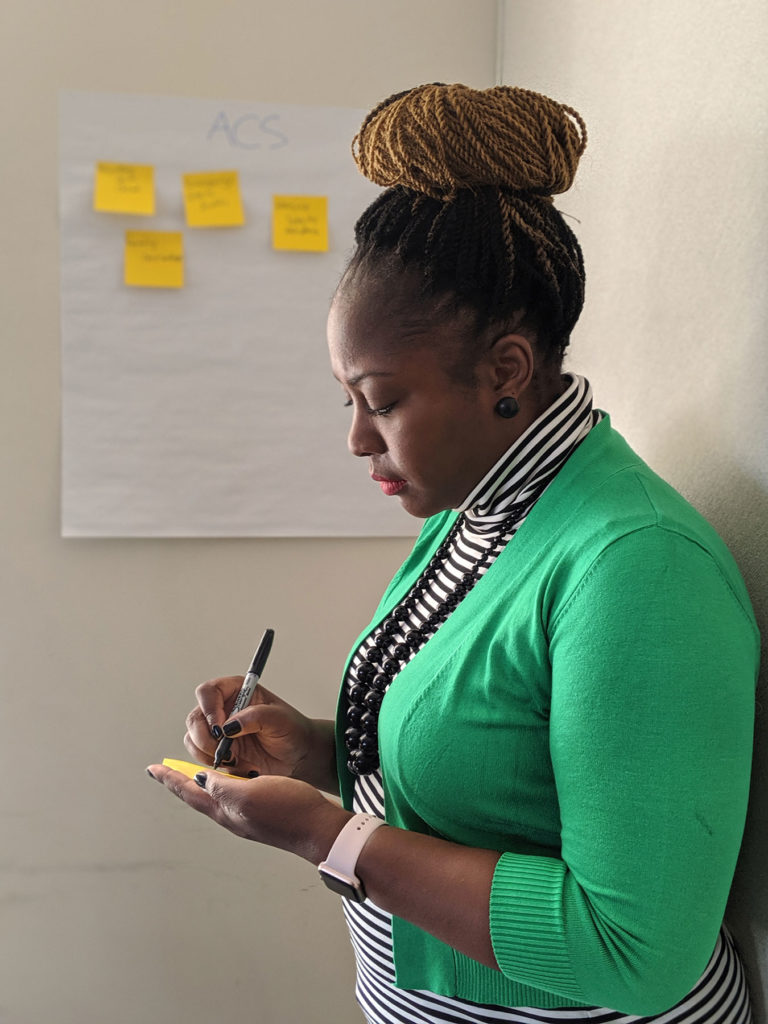 An person writes on a sticky note standing in front of several other sticky notes that have been placed on the wall.