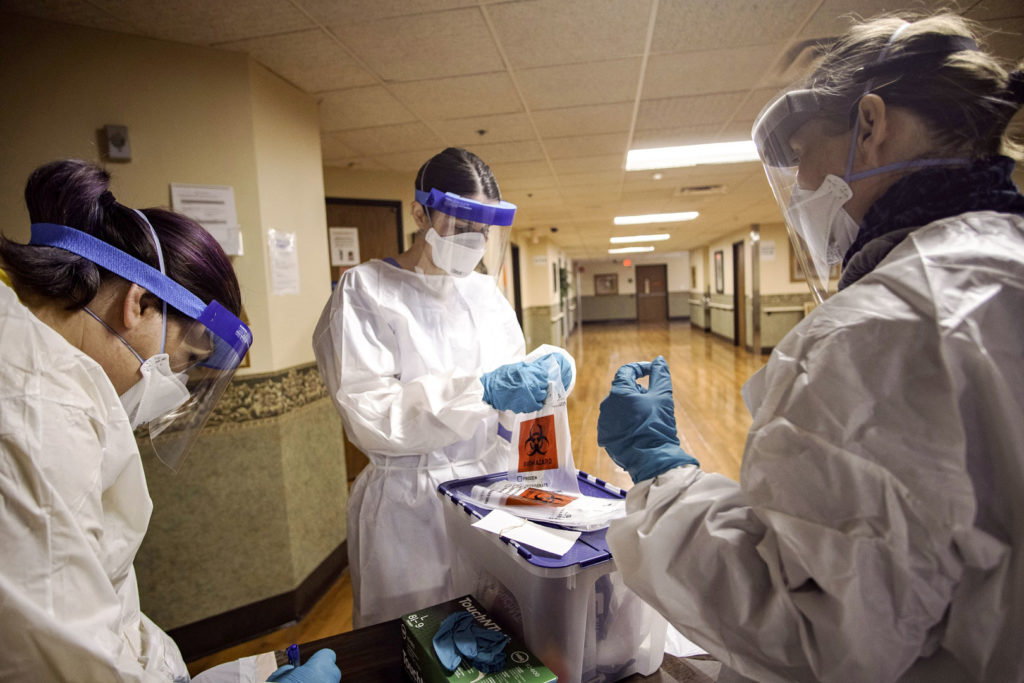 Three infection control employees wearing full-coverage medical protective equipment handle a container of hazardous materials in a hospital.