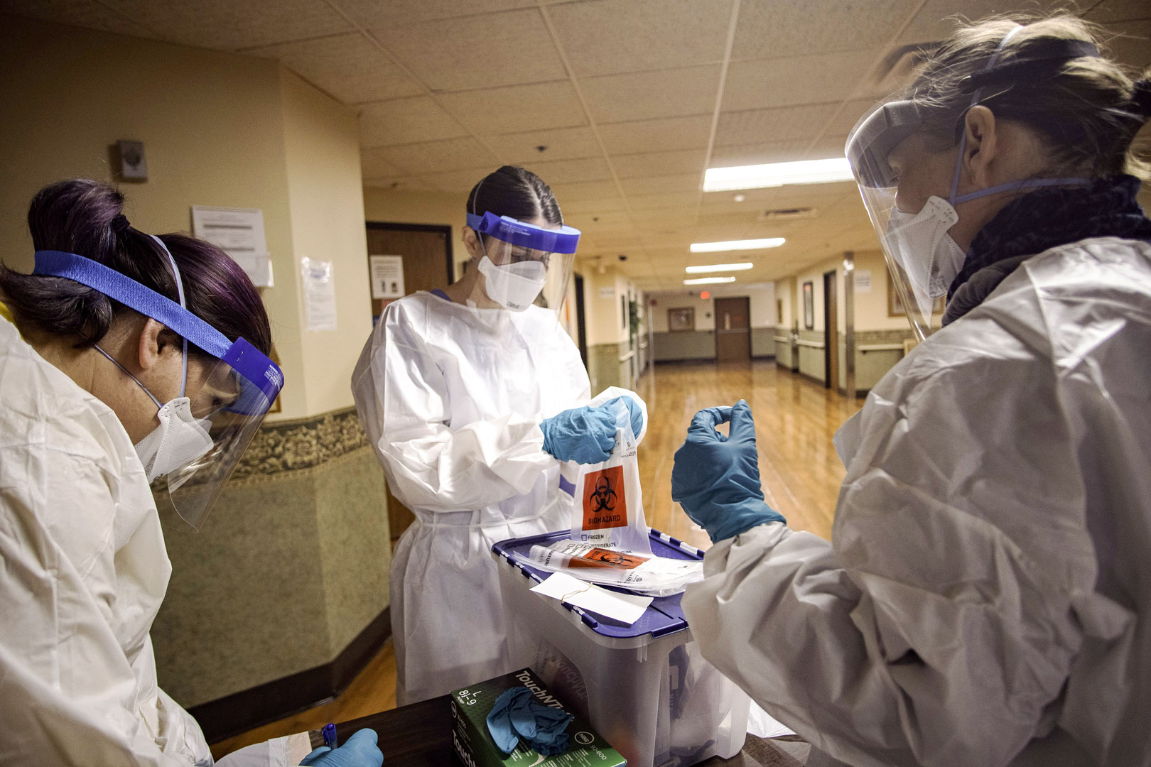Three infection control employees wearing full-coverage medical protective equipment handle a container of hazardous materials in a hospital.