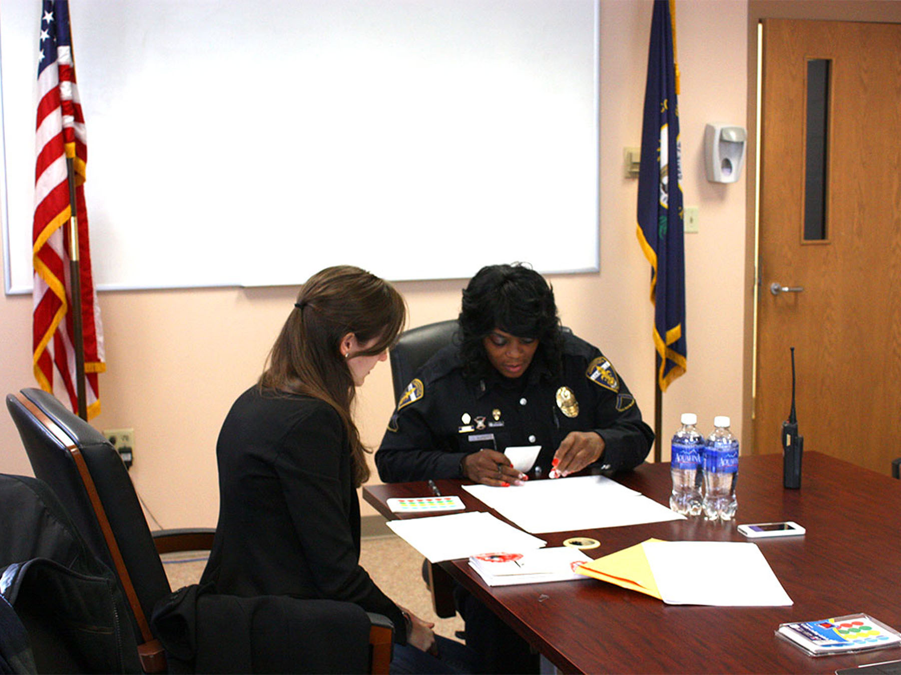 A Public Policy Lab team member talks with a police officer over several documents at a conference table.