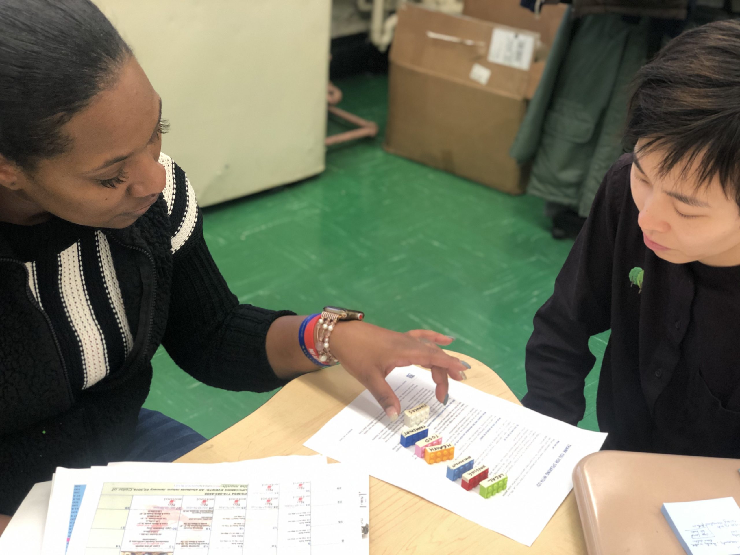 Top-down view of two a researcher and an interviewee sorting through labeled lego pieces on a worksheet-filled table.