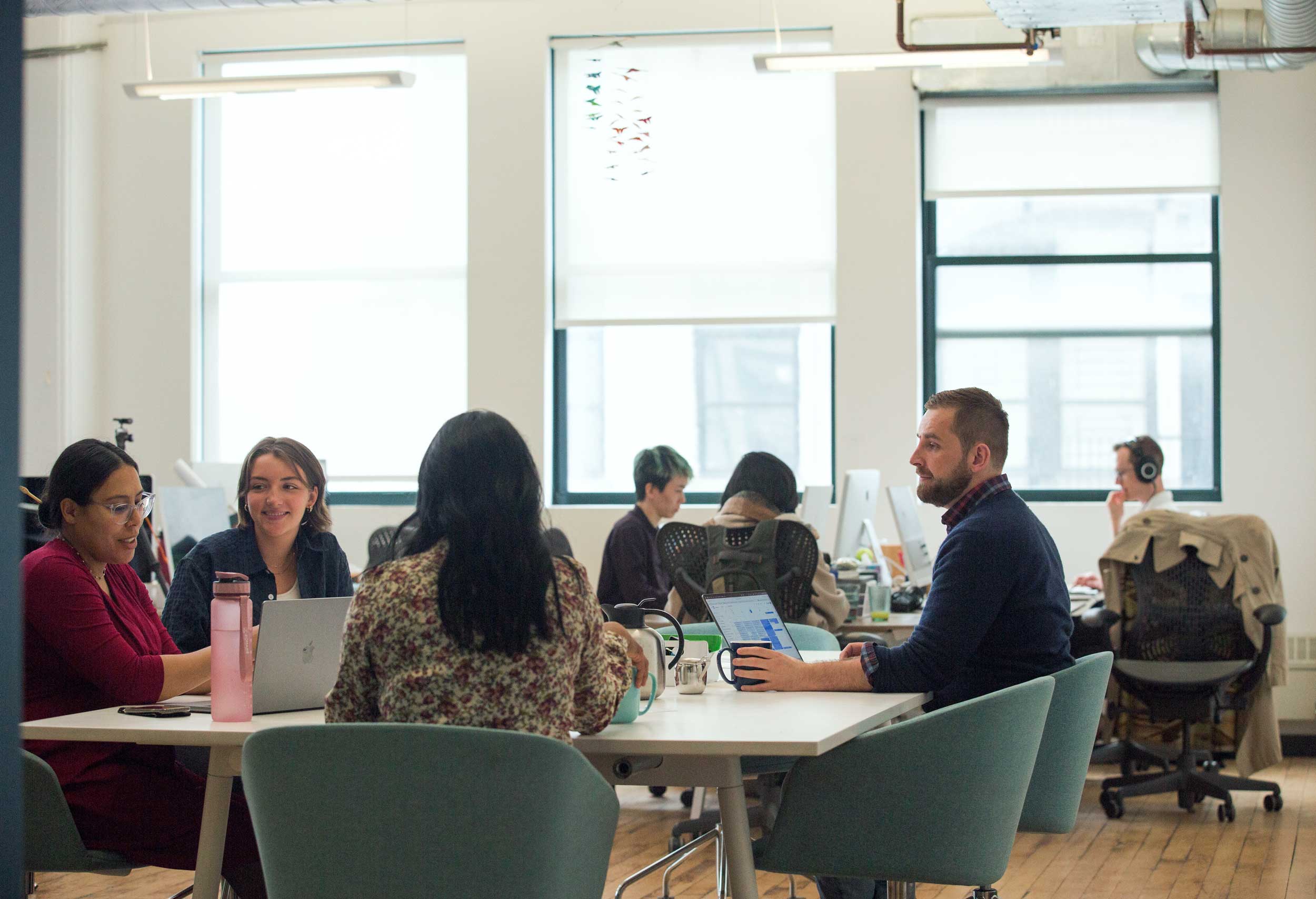 A design team sitting around a large table talking in a sunny office.