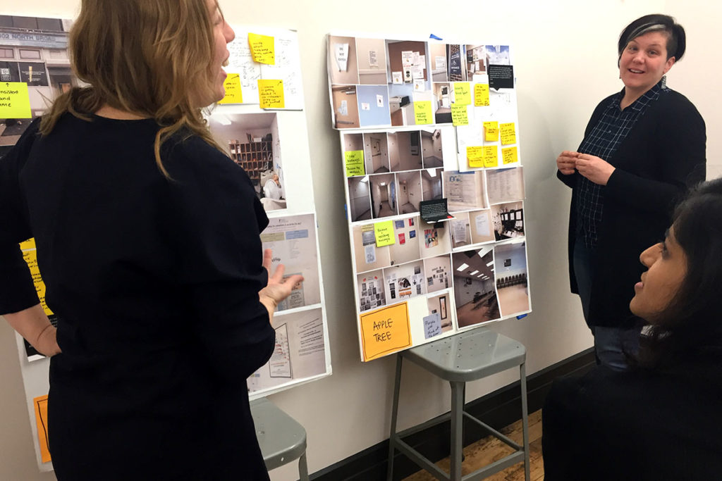 Three individuals discuss two posters filled with photographs and sticky notes.