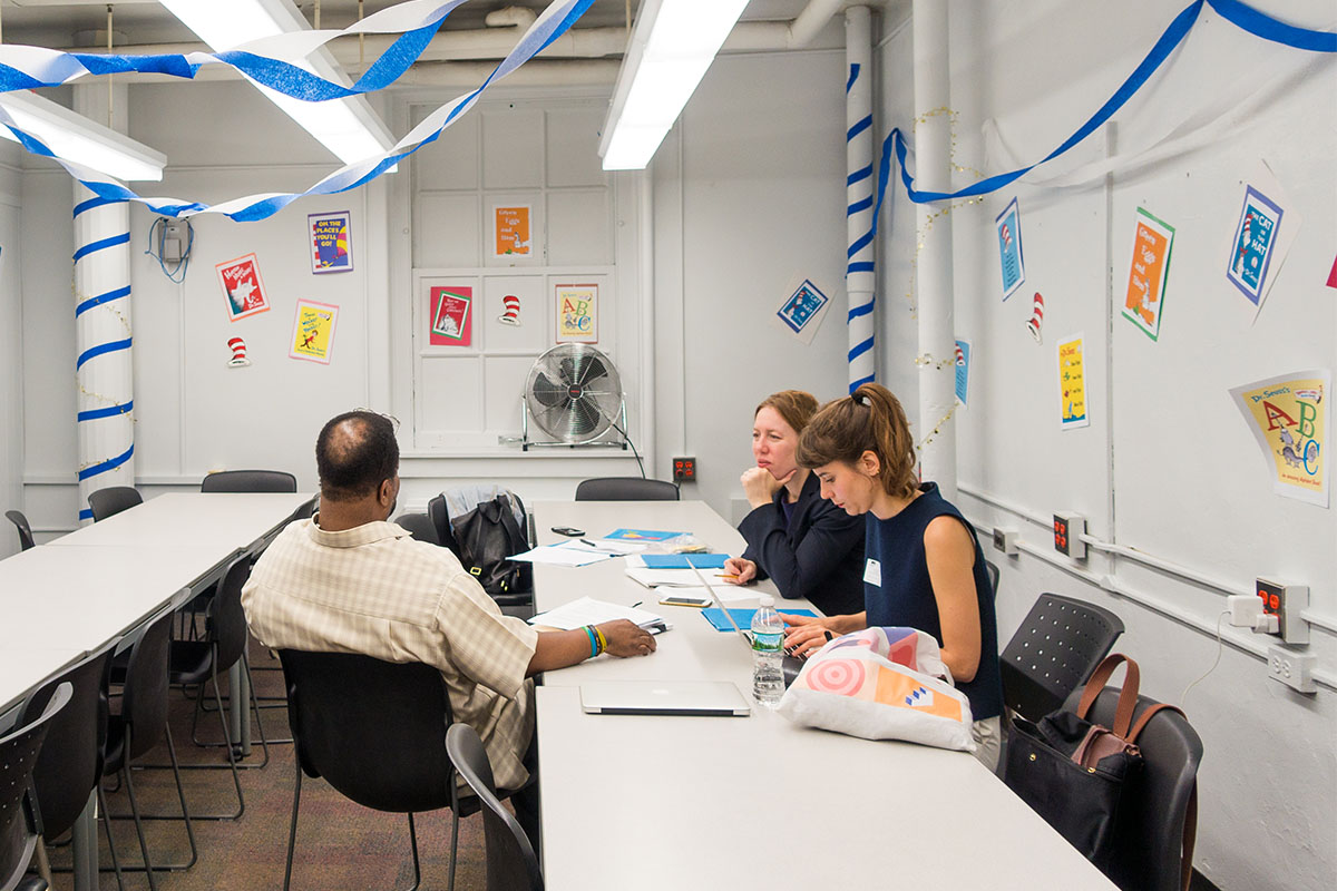 Two PPL team members talk with a collaborator at a long table. The room is filled with streamers hung from the ceiling and images of Dr. Seuss books taped to the walls.