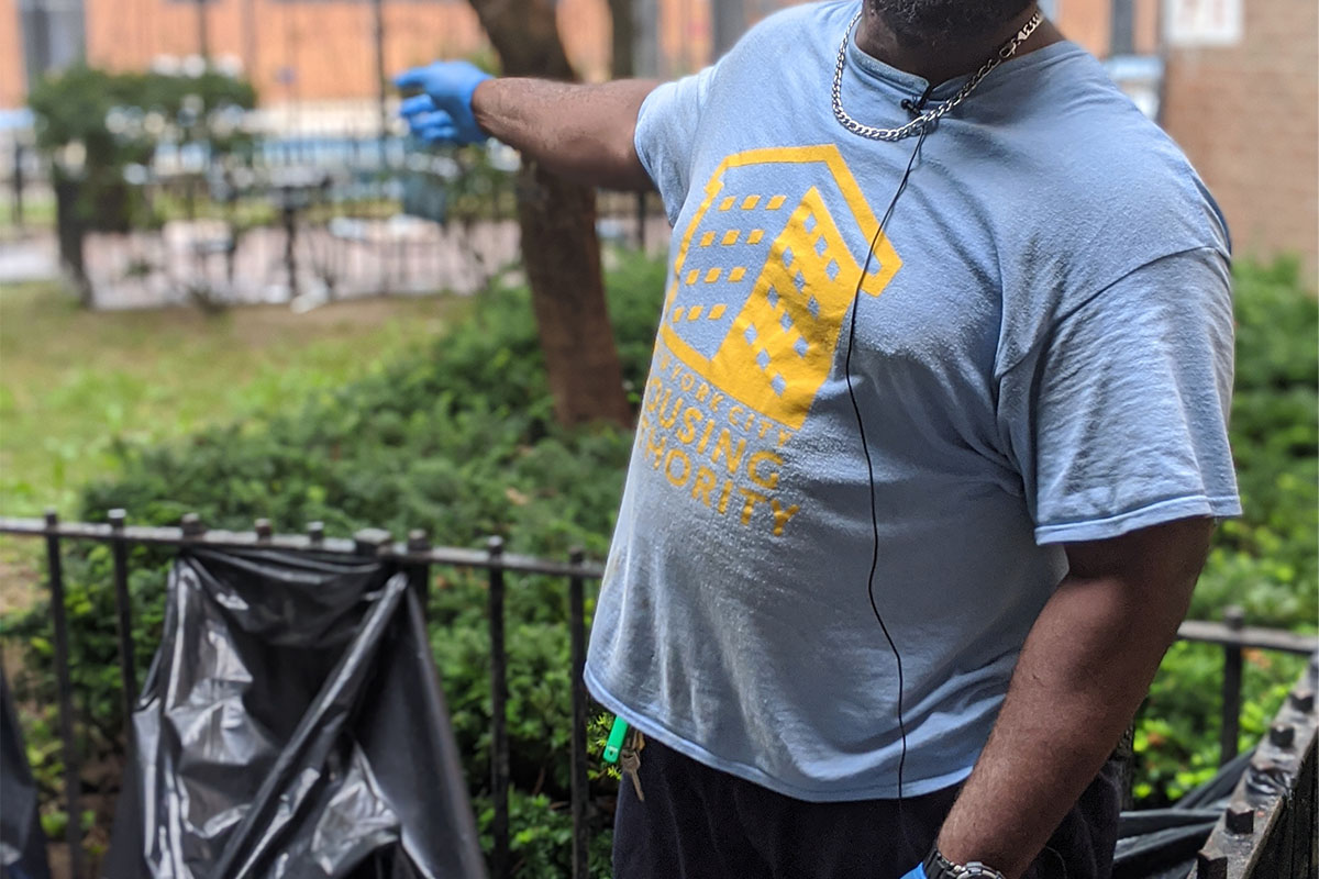 A city employee in a New York City Housing Authority t-shirt collects trash outside of a building.