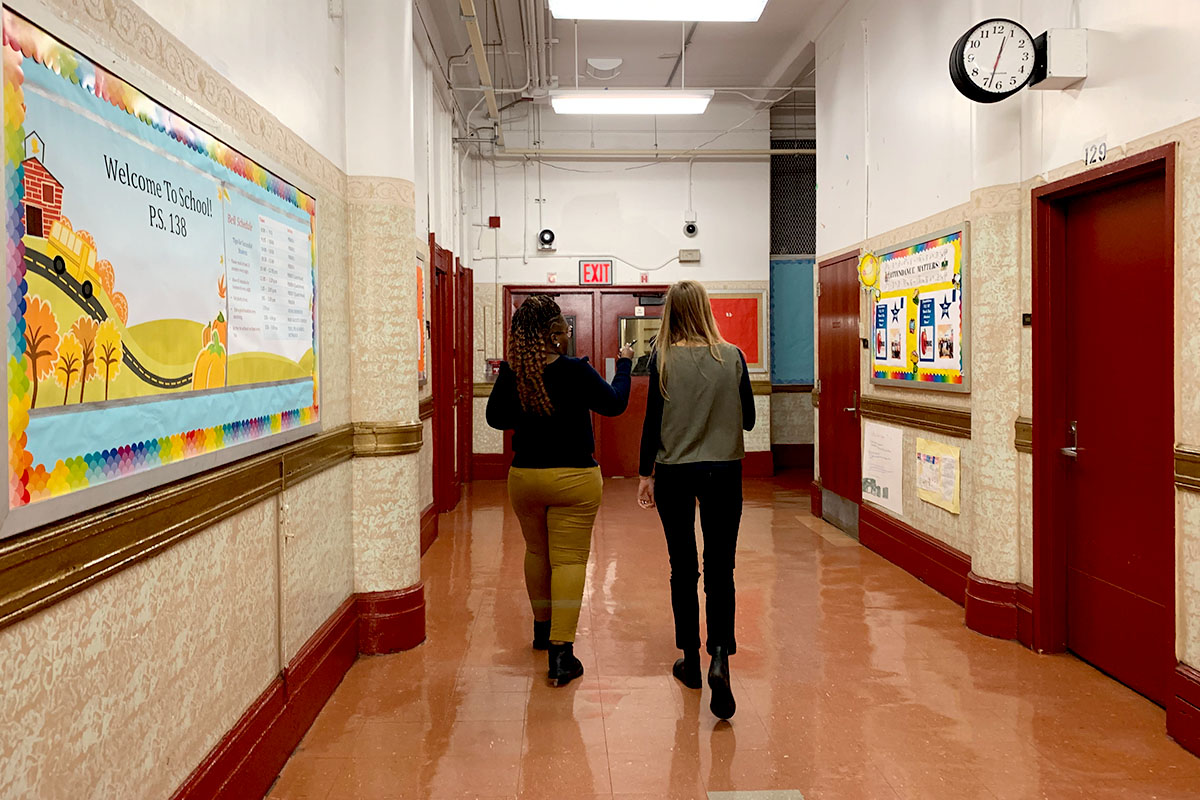Two people walk down a hallway in a New York Public School.
