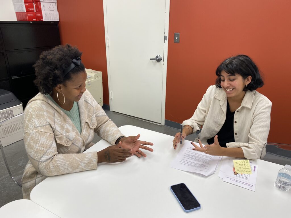 A researcher and a front-line staff have a conversation in the staff member's office. They look together a set of design stimuli.