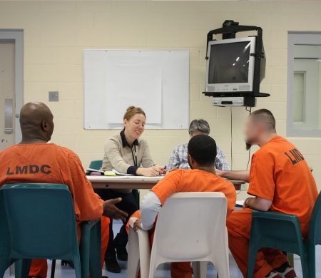 Two PPL team members sit around a table in the Louisville Metro Department of Corrections with three incarcerated individuals. One person takes notes as they talk to each other.
