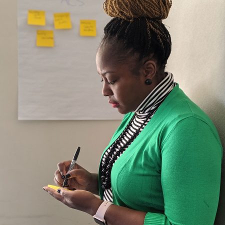 An person writes on a sticky note standing in front of several other sticky notes that have been placed on the wall.