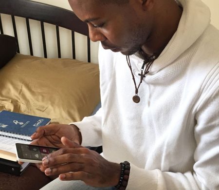 A person sits on a bed looking down at their phone.