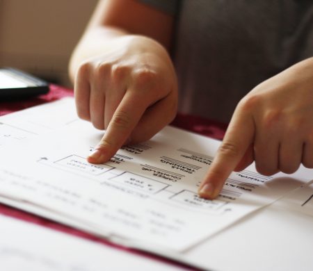 A close up of a person pointing with both hands at different parts of a paper laid out in front of them.