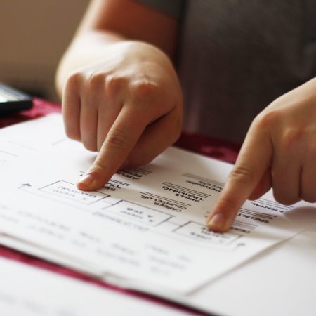 A close up of a person pointing with both hands at different parts of a paper laid out in front of them.