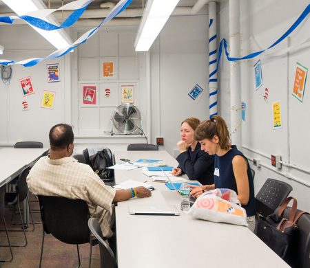 Two PPL team members talk with a collaborator at a long table. The room is filled with streamers hung from the ceiling and images of Dr. Seuss books taped to the walls.