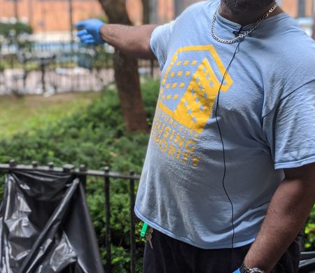 A city employee in a New York City Housing Authority t-shirt collects trash outside of a building.