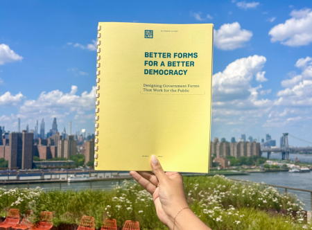 Person's hand holding a publication that says "Better Forms for a Better Democracy"