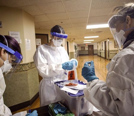 Three infection control employees wearing full-coverage medical protective equipment handle a container of hazardous materials in a hospital.