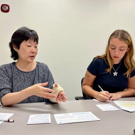 An interviewer sits with a survivor of domestic violence. They are shown gesticulating as they discuss over a set of design stimuli.